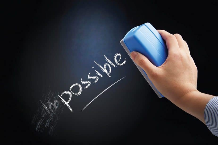A hand uses a blue eraser to remove the "im" from the word "impossible" written in chalk on a blackboard, leaving the word "possible," inspiring unique lesson plan ideas.