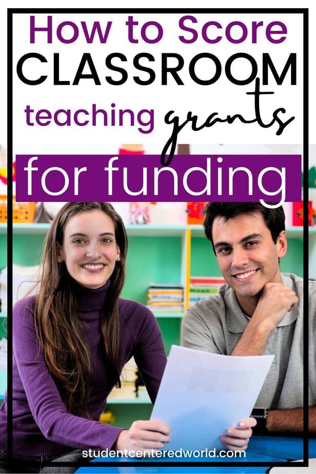 Two teachers, one woman and one man, sit at a desk smiling and holding papers in a colorful classroom. Text on image reads: How to Score Teaching Grants for Classroom Funding.
