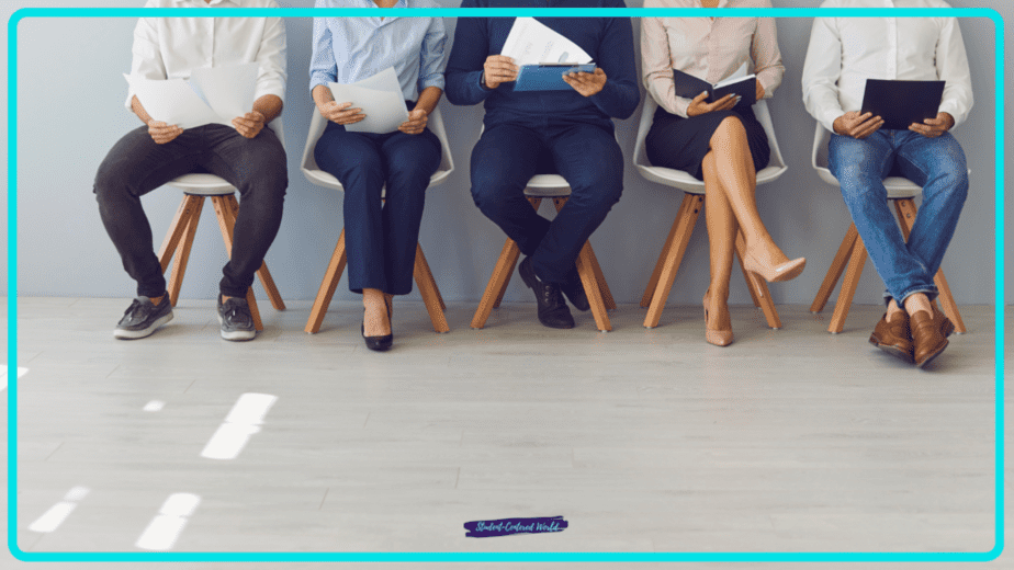 Five individuals sit in chairs against a wall, each holding resumes or papers, dressed in business casual attire. The scene suggests a waiting room setting for teacher interview questions, highlighting the anticipation and preparation typical of job interviews.