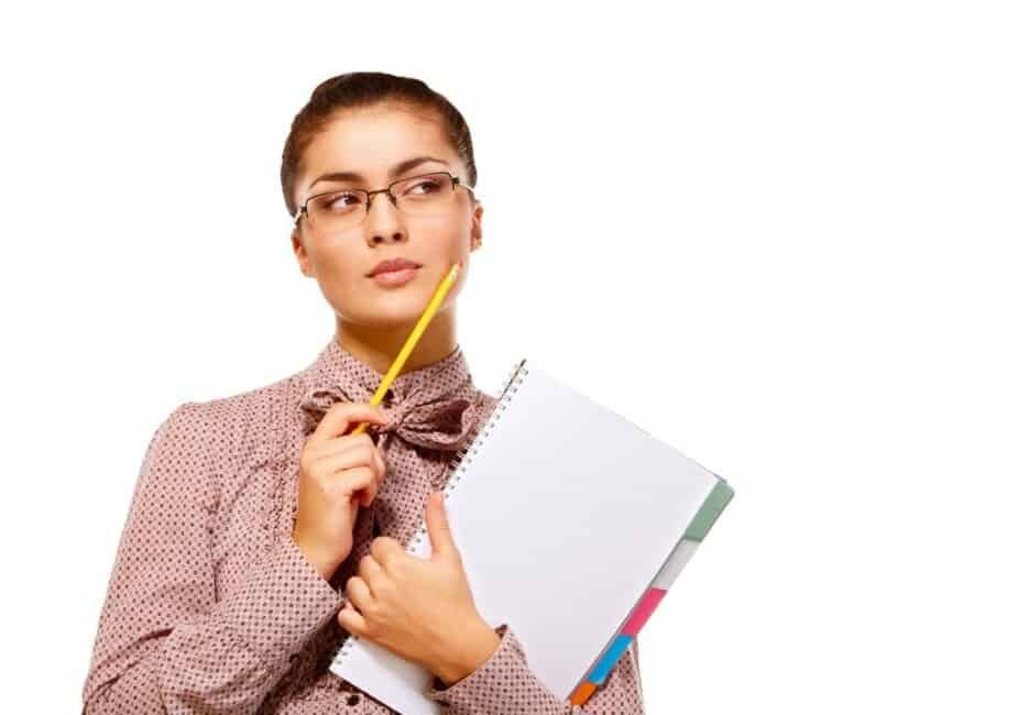 A woman wearing glasses and a patterned blouse holds a notebook and a yellow pencil while looking thoughtfully to the side against a white background.